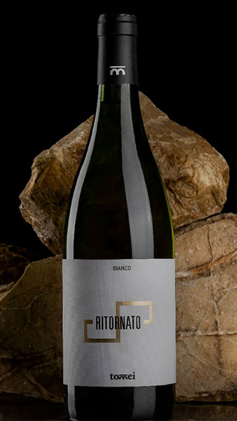 Bottle of Ritournato wine from Tomei in front of vineyard rocks